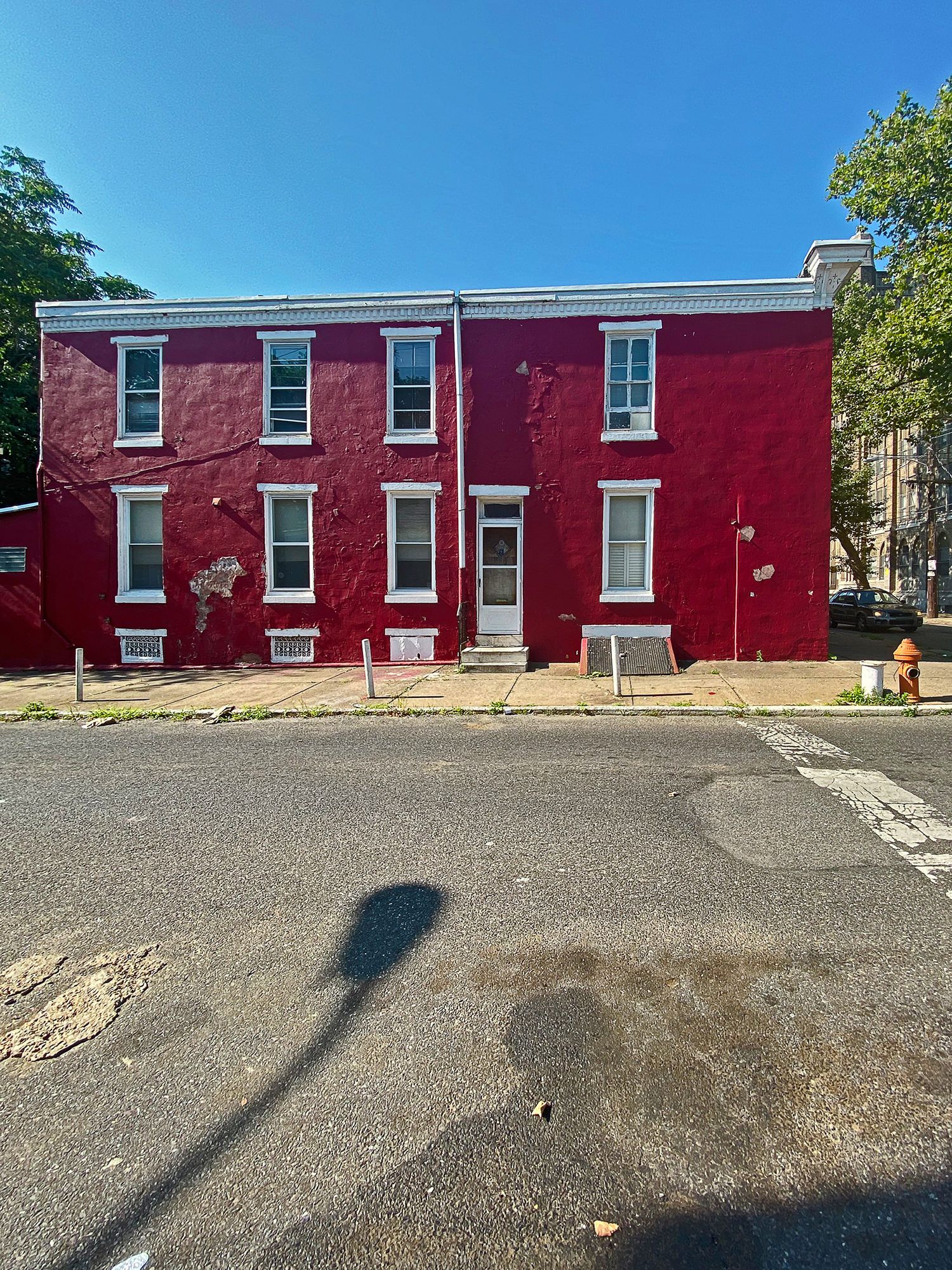Image description: a photograph showing the exterior of the artist’s home where she grew up, a red two-story apartment building, with cement in the foreground and a blue sky and trees on both sides of the building. Art by Deborah Willis.